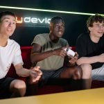 Three young men having fun playing video games together on a sofa. — Experience Fun and Secure Gambling with Toto Playground