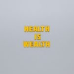 Inspirational phrase 'Health is Wealth' in bold yellow letters on a neutral gray background. — Facial, Body Wrap, or Massage?