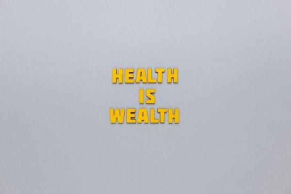Inspirational phrase 'Health is Wealth' in bold yellow letters on a neutral gray background. — Facial, Body Wrap, or Massage?