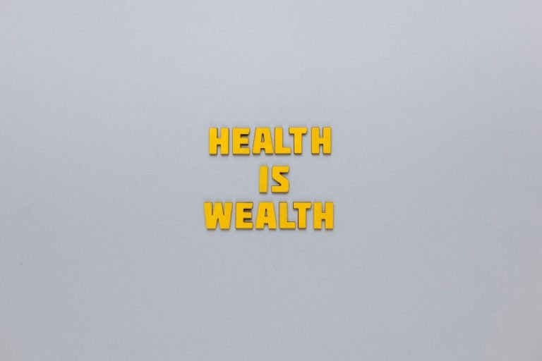 Inspirational phrase 'Health is Wealth' in bold yellow letters on a neutral gray background. — Facial, Body Wrap, or Massage?