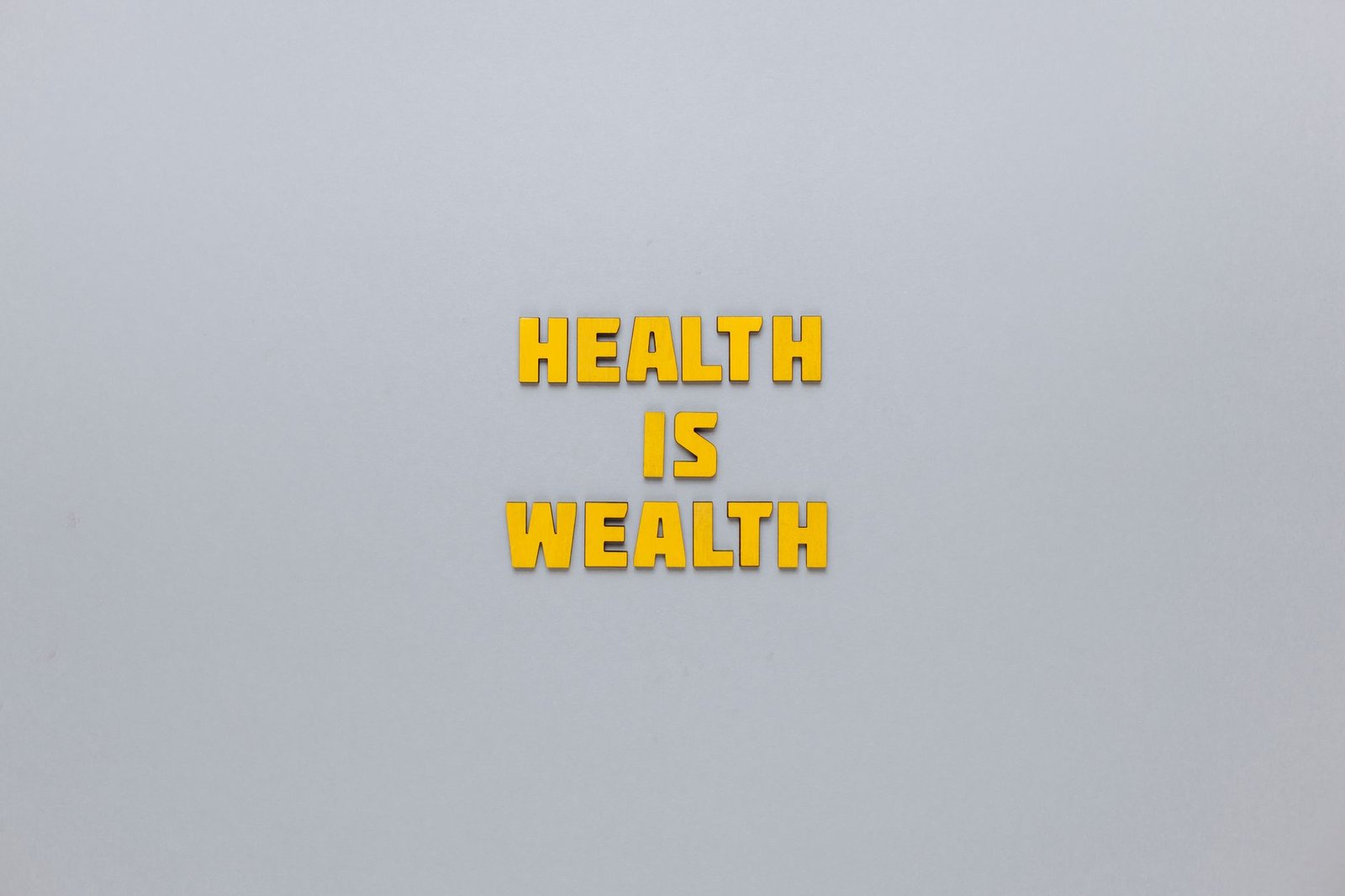 Inspirational phrase 'Health is Wealth' in bold yellow letters on a neutral gray background. — Facial, Body Wrap, or Massage?