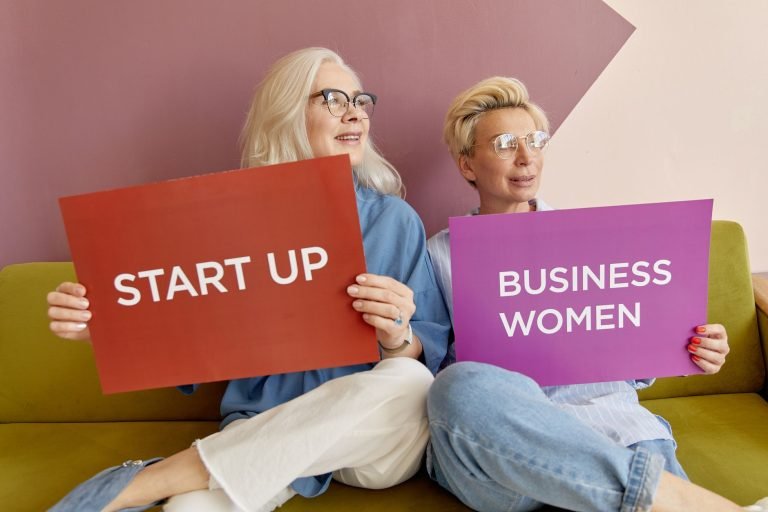 Two women on a sofa holding signs promoting startup and business women. — Mastering the Balance: How Modern Mothers Can Thriv